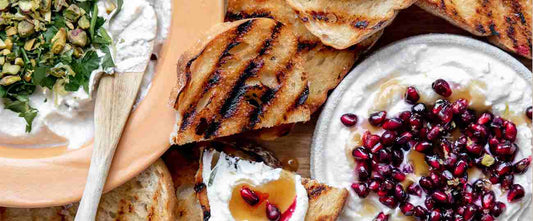bowl of whipped ricotta with pine nuts and pomegranate arils and piece of toast on the side
