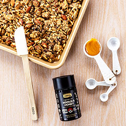 granola on a baking tray with jar of honey and cooking utensils