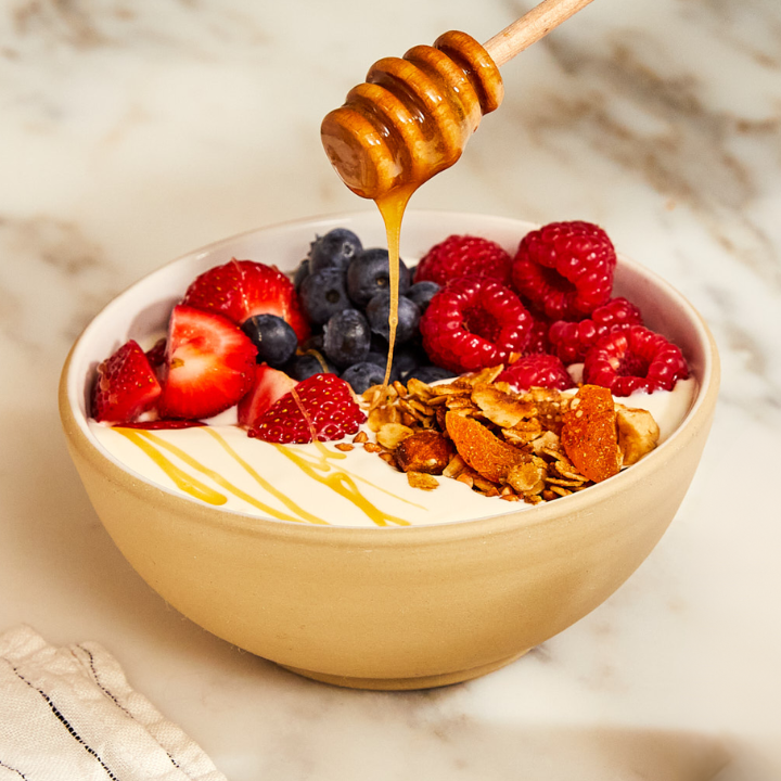 bowl of yogurt berries and honey on a spoon