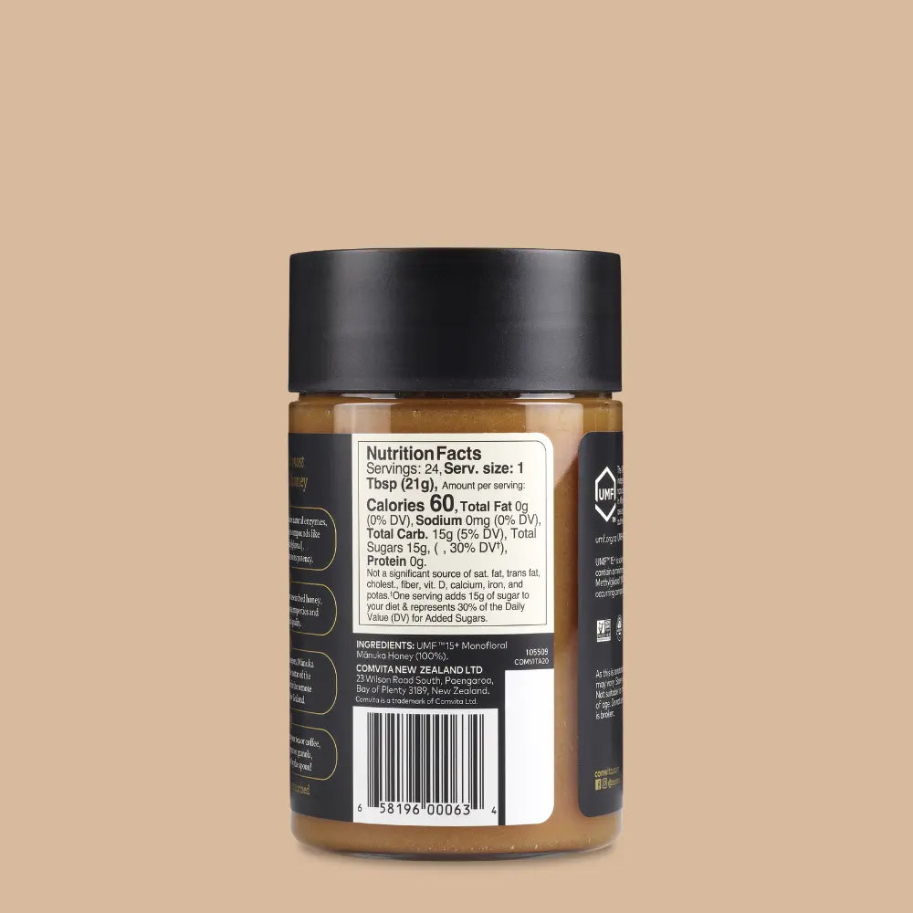 Jar of Comvita Manuka honey with a black lid on a beige background