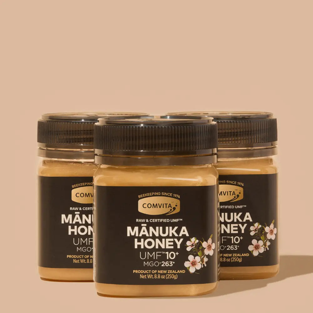 Three jars of Comvita Manuka Honey on a beige background