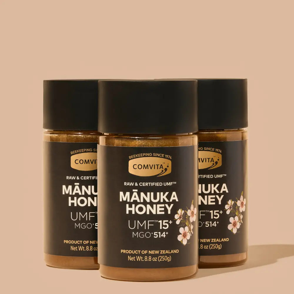 Three jars of Manuka honey with Comvita branding on a beige background
