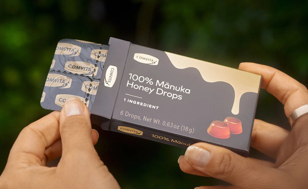 Box of 100% Manuka Honey Drops held by hands with a blurred green background