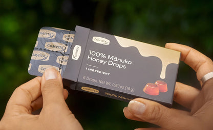 Box of 100% Manuka Honey Drops held by hands with a blurred green background