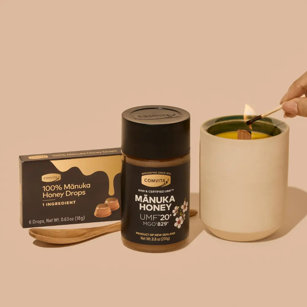 Manuka honey jar with a box of honey drops, candle and a wooden honey spoon on a beige background