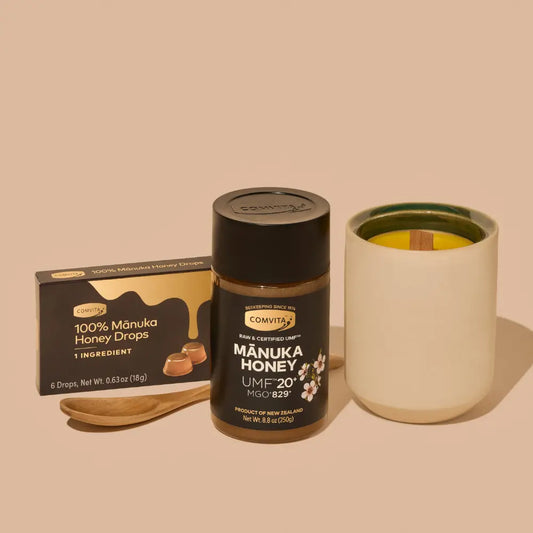 Manuka honey jar with a box of honey drops, candle and a wooden honey spoon on a beige background