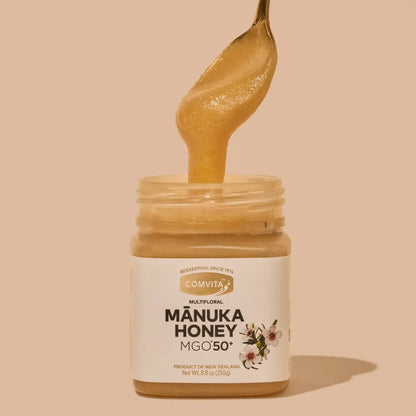 Jar of Comvita Manuka Honey with a spoonful of honey on a beige background