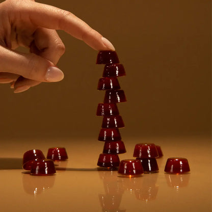 Hand stacking Manuka Honey drops on a reflective surface with a warm brown background