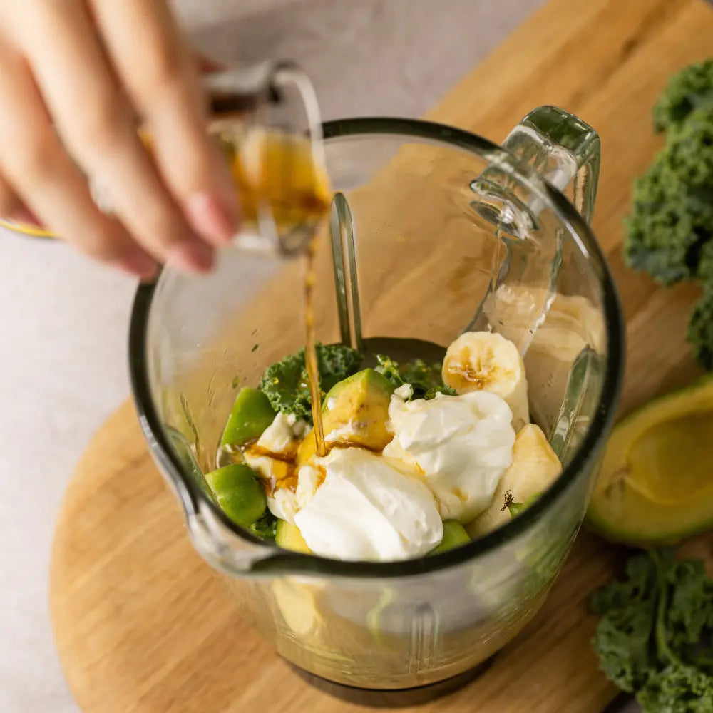 Hand pouring Olive Leaf Extract into a blender with ingredients on a wooden board