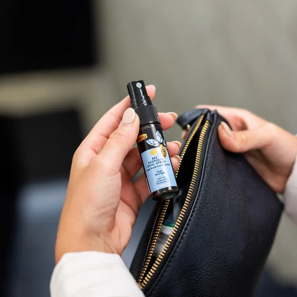 Person holding Comvita Bee Propolis Throat spray bottle labeled next to an open black leather purse.