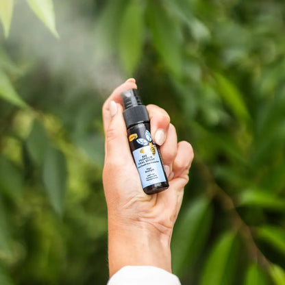 Hand holding Comvita Bee Propolis Throat Spray bottle with a green leafy background