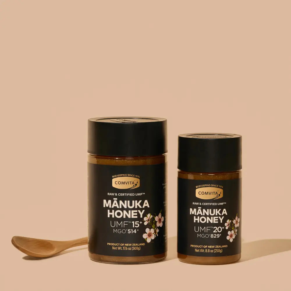 Two jars of Manuka honey with a wooden honey spoon on a beige background