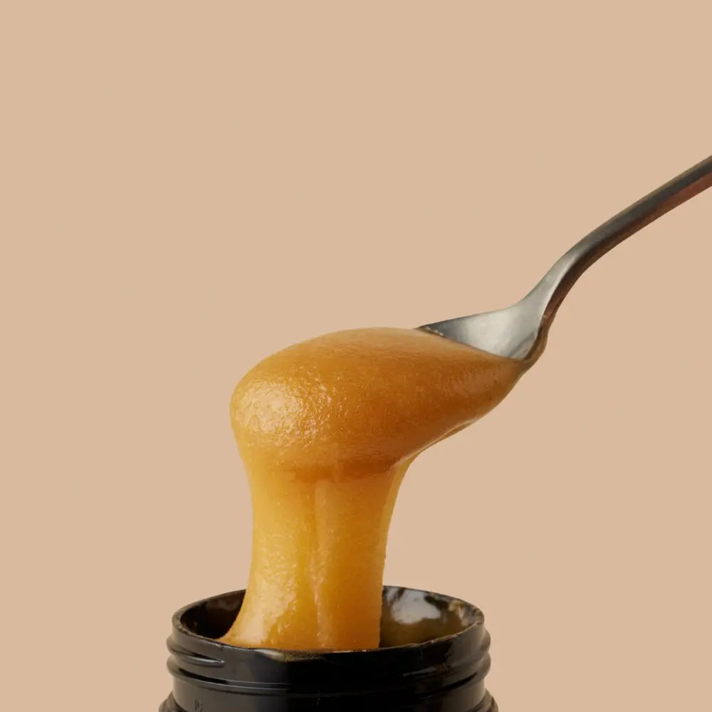 spoonful of Manuka Honey on spoon coming out of a jar on a beige background