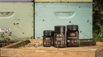 3 umf manuka honey jars with bees and bee boxes in backround