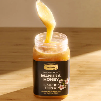 Jar of Comvita Manuka Honey with a spoonful being poured on a wooden surface