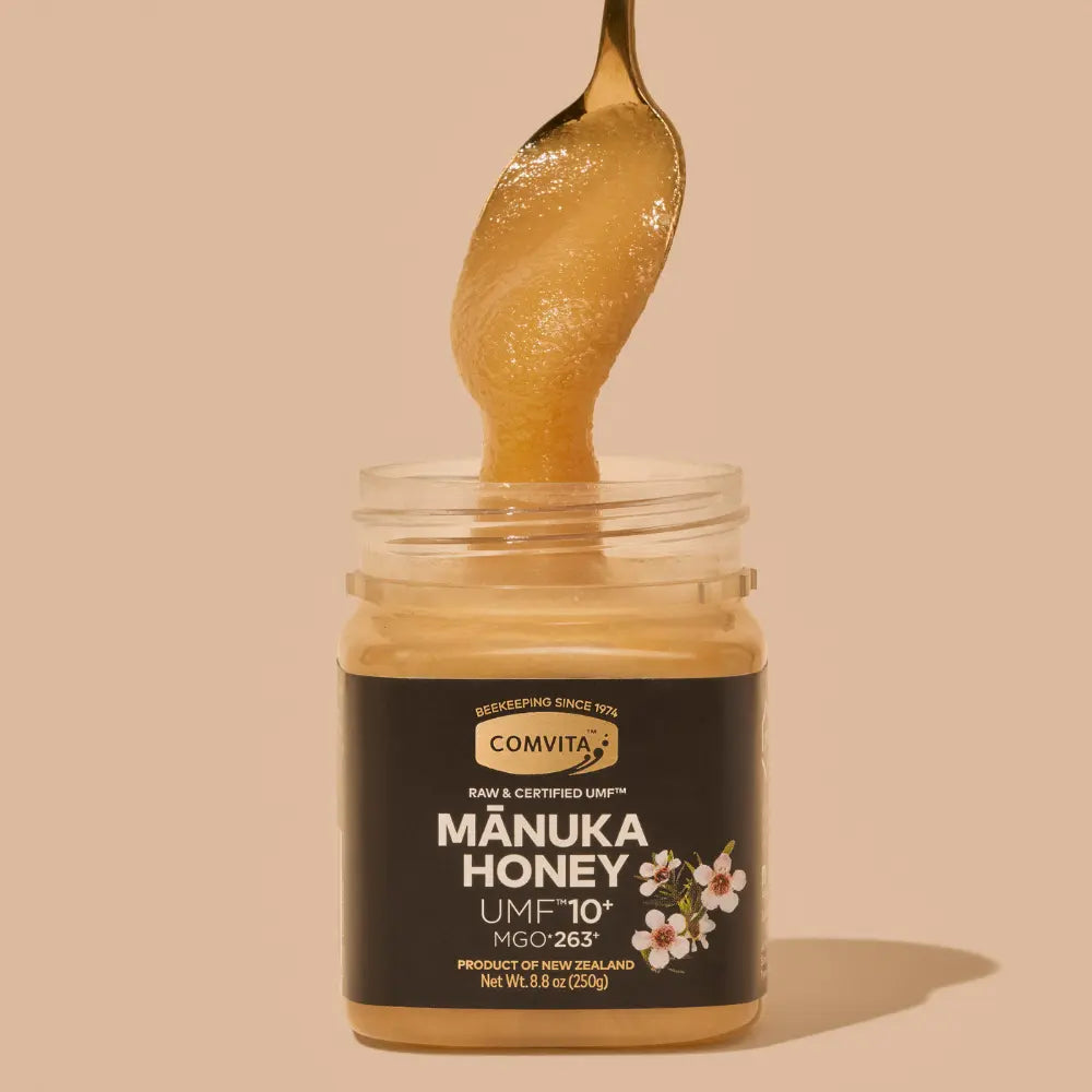 Jar of Comvita Manuka Honey with a spoonful of honey on a beige background