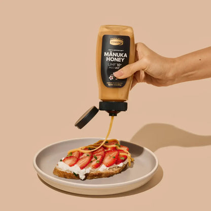 Hand pouring Manuka Honey onto a plate with strawberries and toast on a beige background