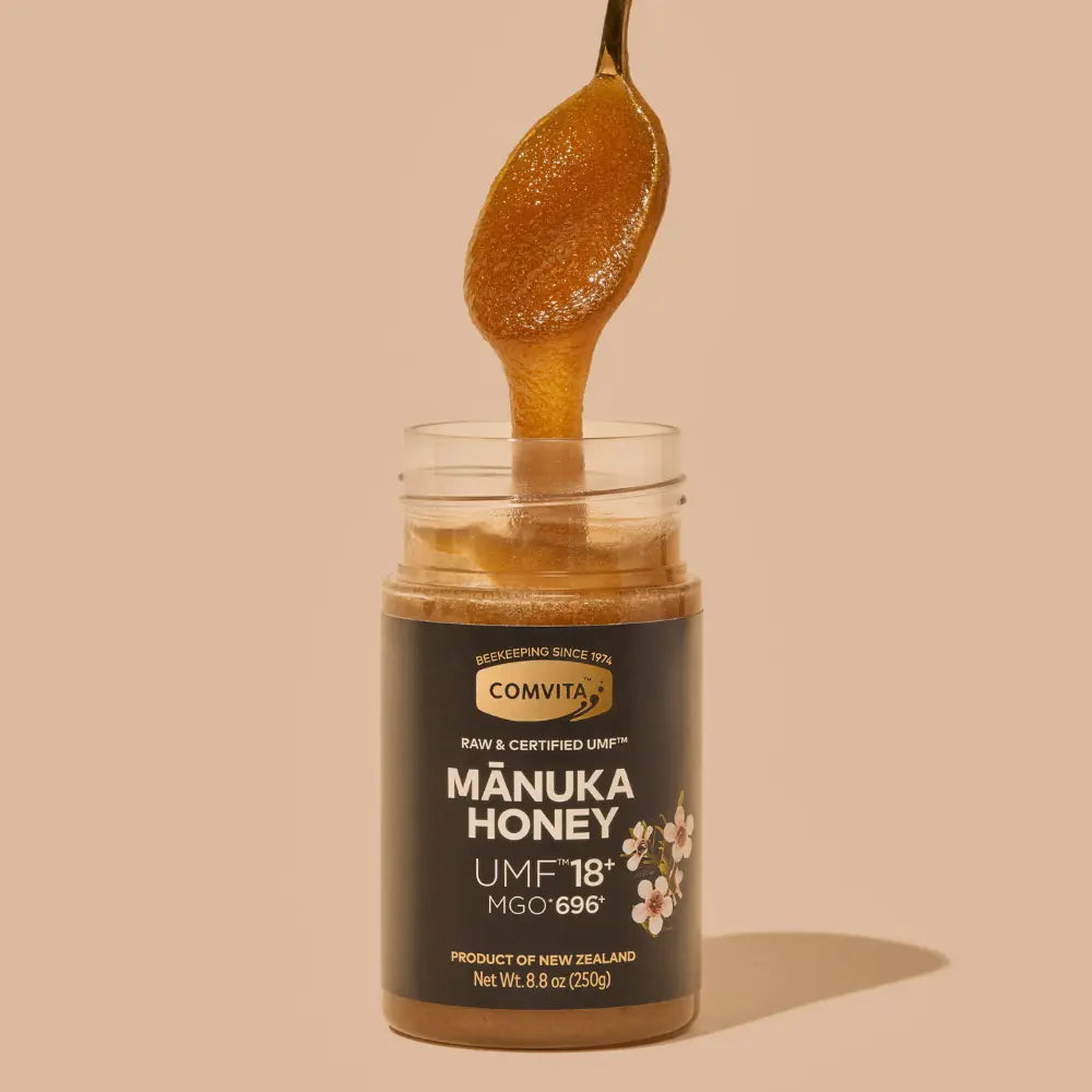 Jar of Comvita Manuka Honey with a spoonful of honey on a beige background
