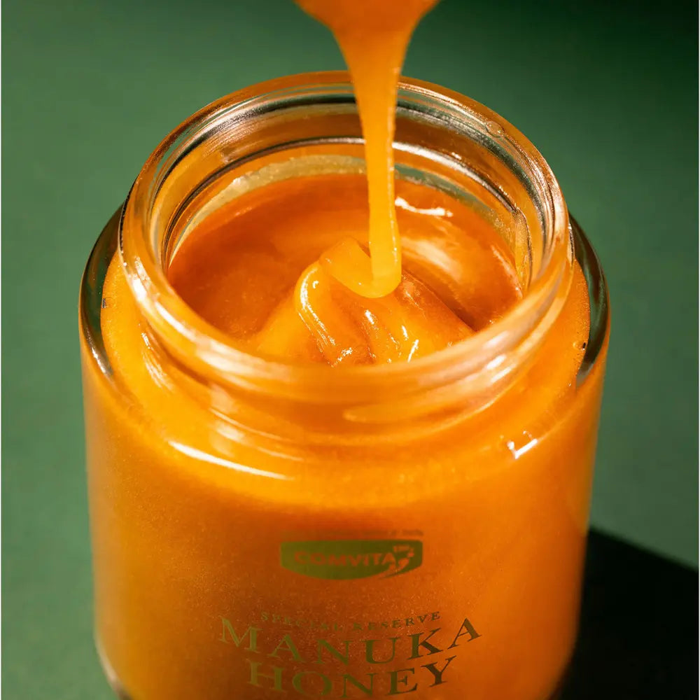 Manuka honey being poured into a jar with a green background