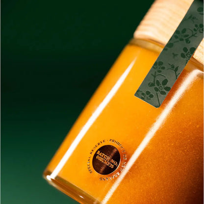 Close-up of a jar with a green label and gold emblem on a dark green background