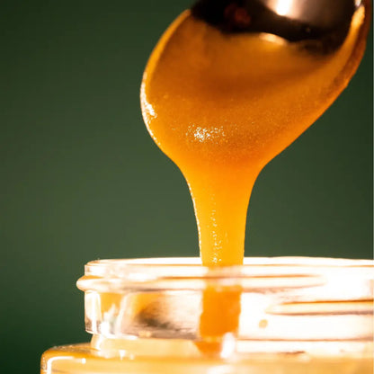 Manuka honey being drizzled from a spoon into a jar with a green background