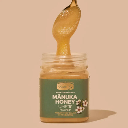 Jar of Comvita Manuka Honey with a spoonful of honey on a beige background