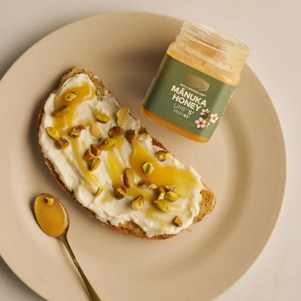 Manuka honey jar on a plate with honeycomb and honey drizzled on a piece of toast.