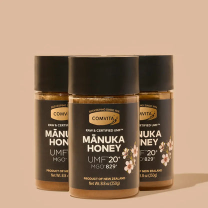 Three jars of Manuka honey with Comvita branding on a beige background