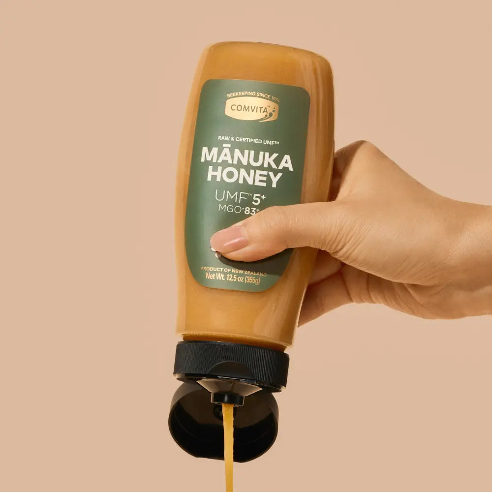 Hand holding a squeeze bottle of Comvita Manuka Honey against a beige background