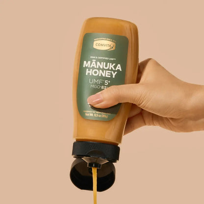 Hand holding a squeeze bottle of Comvita Manuka Honey against a beige background