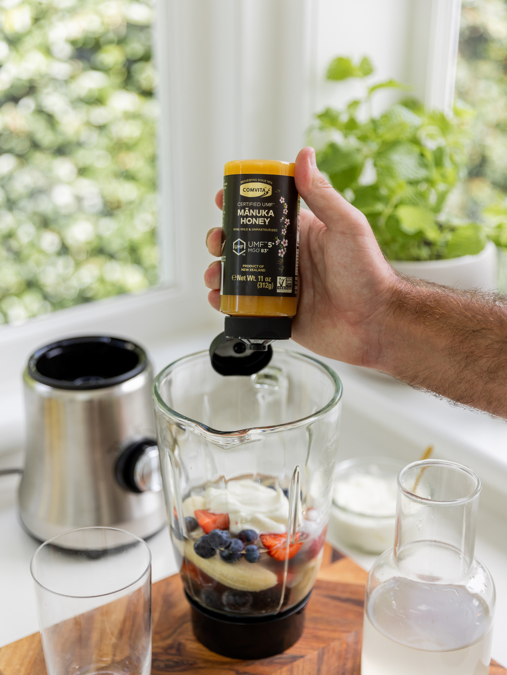 a man adding manuka honey from a squeezy bottle to a smoothy